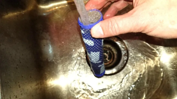 The Dyson v6 filter being rinsed out with water in a sink.